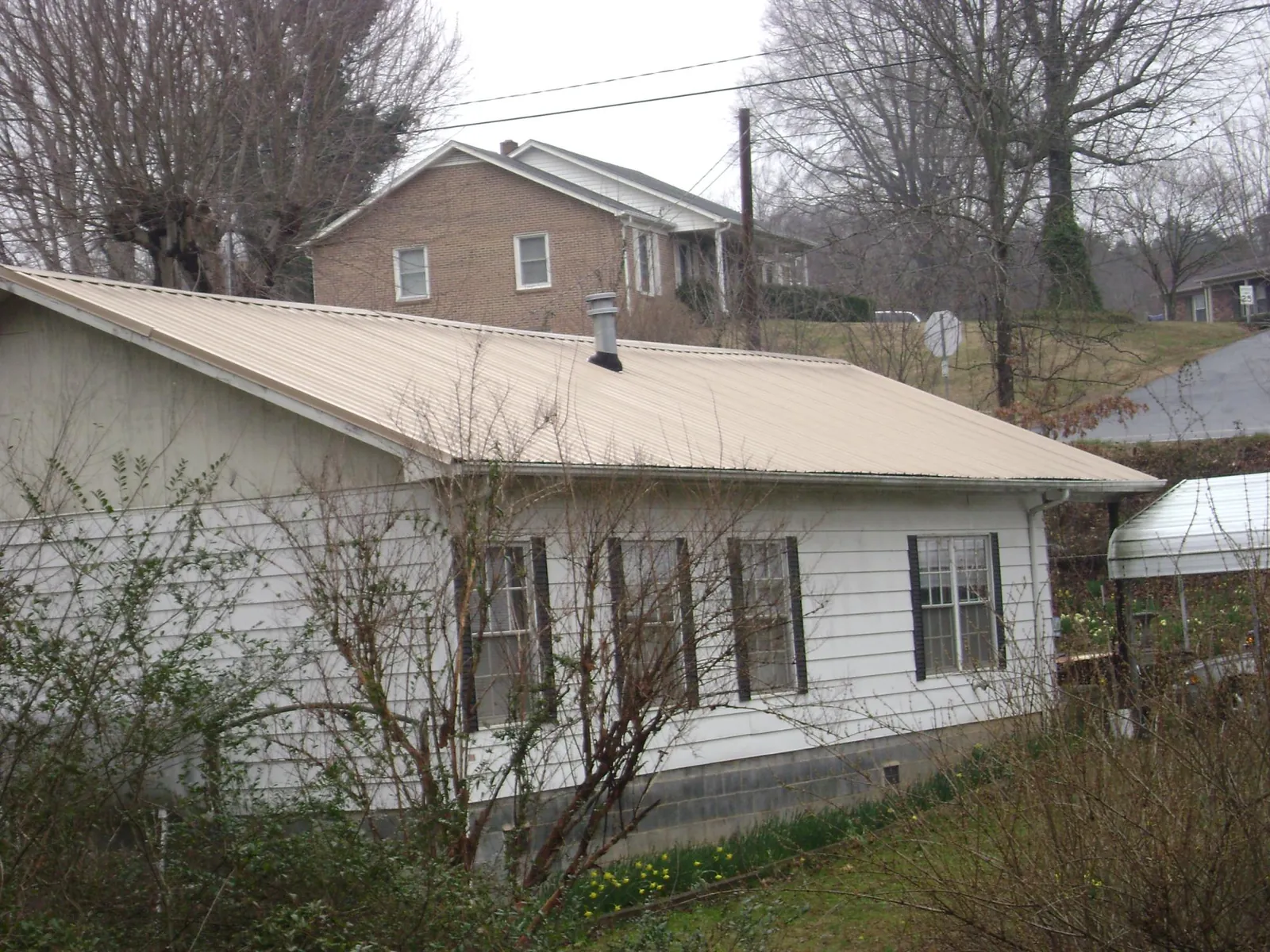 Tan metal roof on a white sided house set into a hillside — Commercial Roofing by Roofing Brothers in Fayetteville